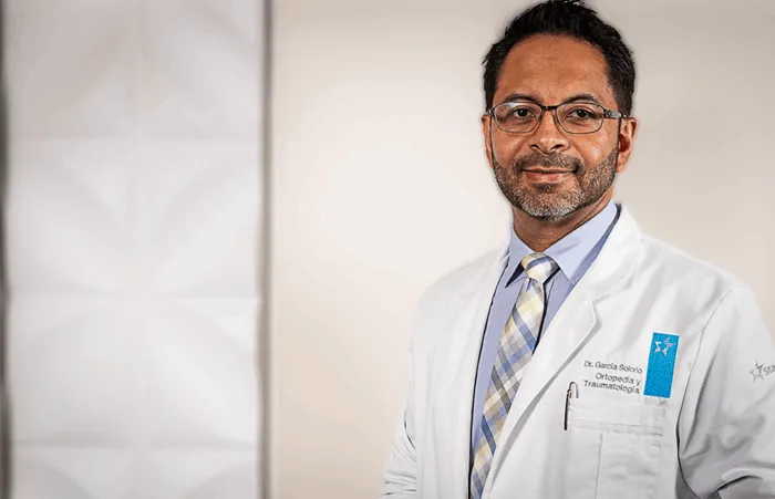 traumatologo_retrato_profesional_bata_dr_garcia_solorio_queretaro_700x451 Retrato profesional del Dr. Alfonso García Solorio, especialista en traumatología, con bata médica y expresión confiada.